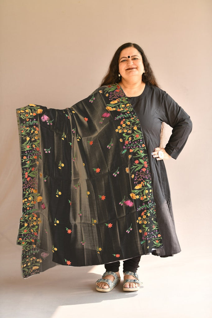 Front view of model wearing a Black Chanderi Silk dupatta shawl with big hand-painted and printed floral meadows and motifs in bright colourful colours.
